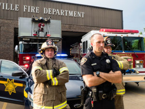 Firefighters and police officers standing in front of fire station and vehicles