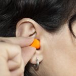 A Woman Inserts An Orange Silicone Plug In Her Ear To Avoid Anno