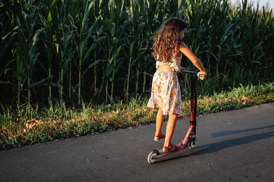 Girl In Flower Dress Riding Red Scooter On A Country Road Next T
